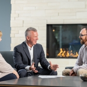 Three Twin Feathers employees sit around table with fireplace in background and discuss marketing strategy.