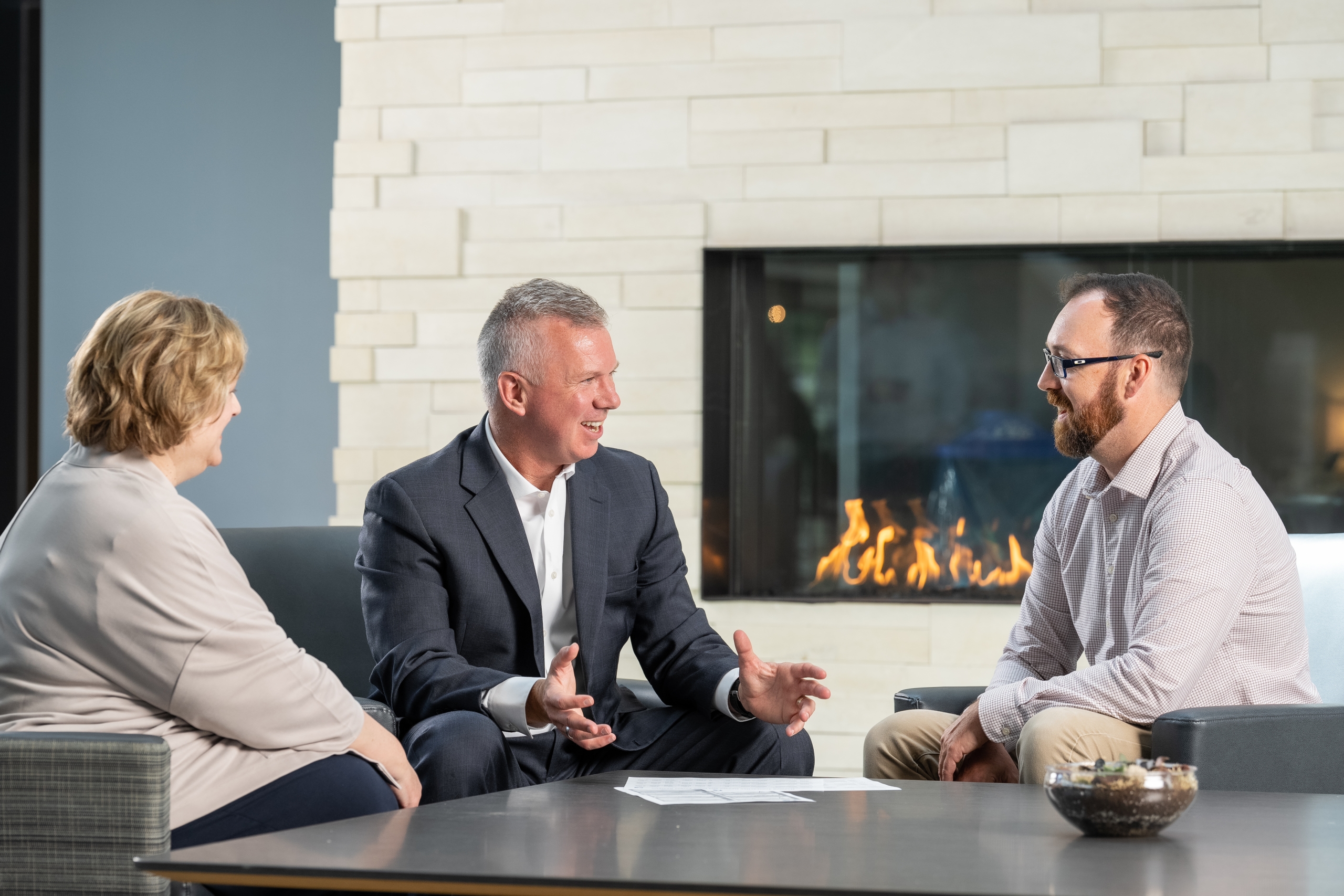 Three Twin Feathers employees sit around table with fireplace in background and discuss marketing strategy.