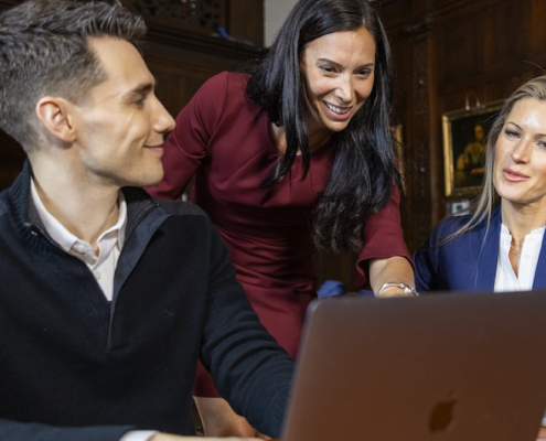 Female training instructor discussing training materials with two attendees who are seated on their laptops.