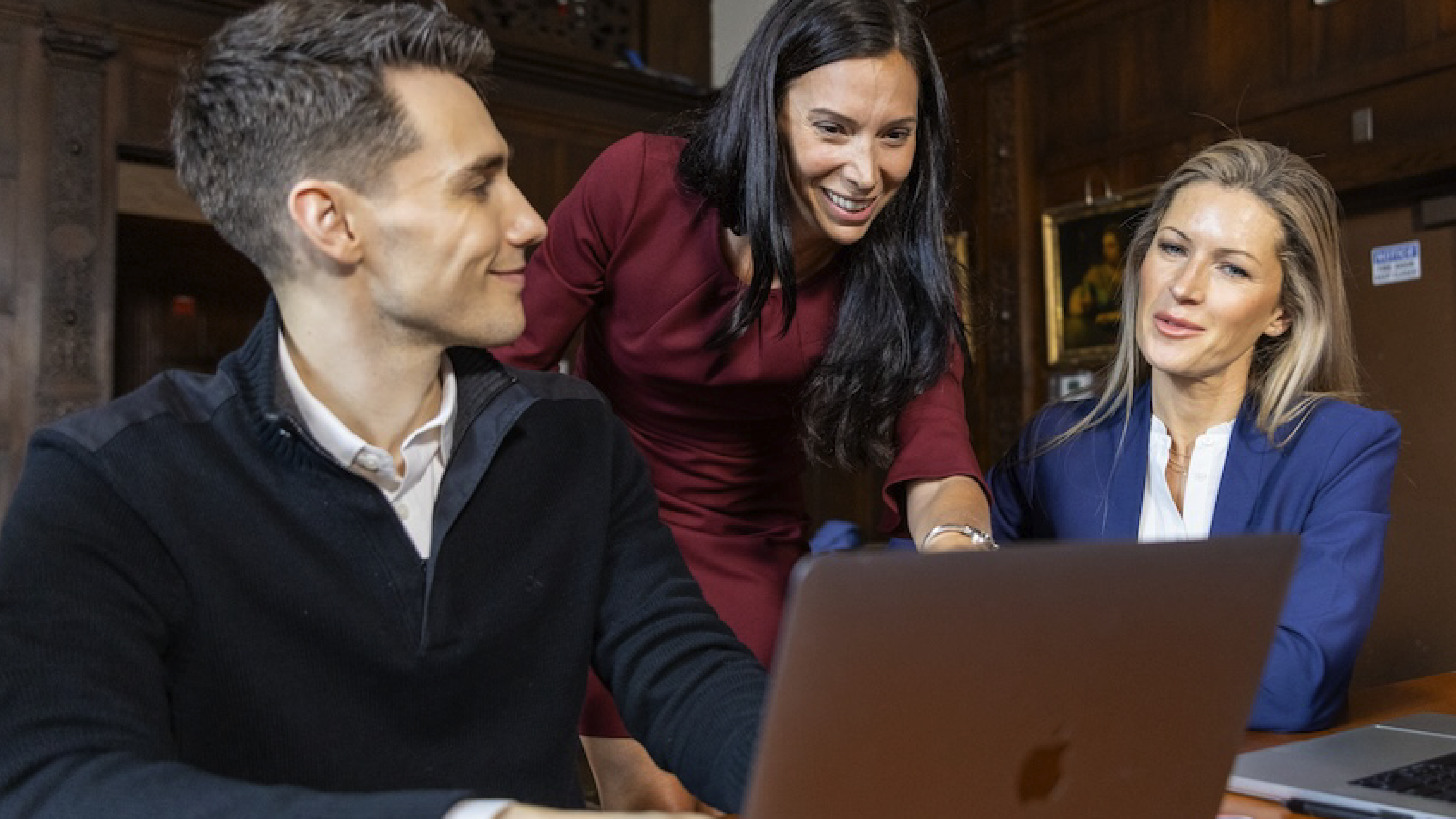 Female training instructor discussing training materials with two attendees who are seated on their laptops.